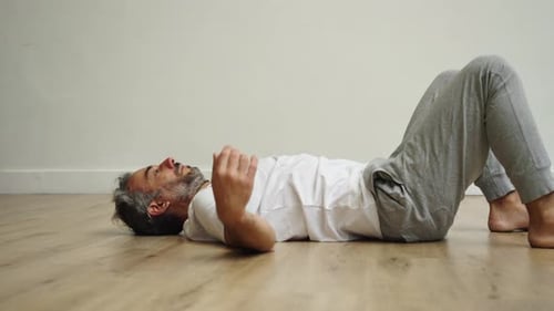 Man Stretches and Exercises Indoors on Wood Floor