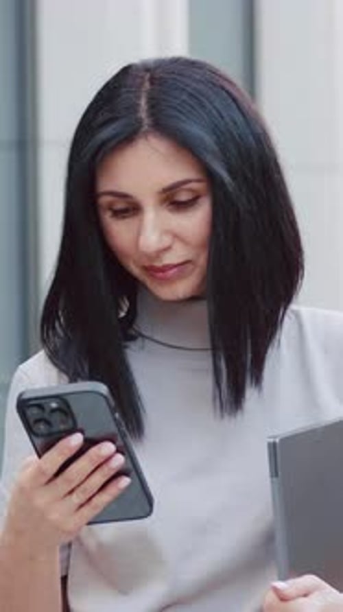 Young Caucasian Business Woman Using Cell Phone Mobile App and Holding Computer Device for Work