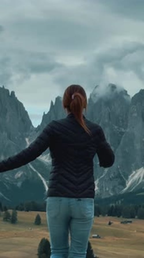 woman from behind spreading her arms wide, embracing the mountain landscape of the Dolomites
