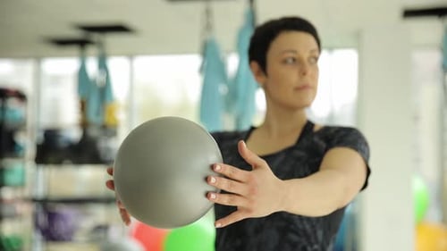 Athletic Woman Purposefully Performs Various Exercises with a Ball in a Modern Fitness Studio