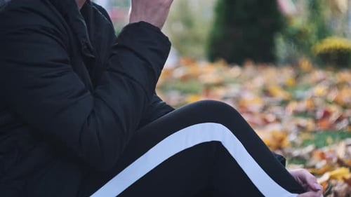Young Woman Drinks Coffee on Lawn in Autumn Park Among Fallen Yellow Leaves