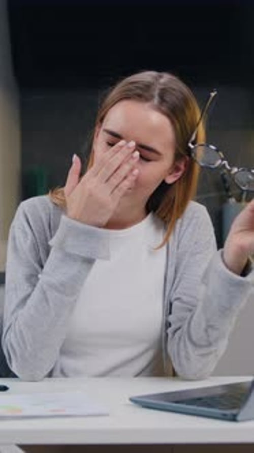 Young Woman Sitting at Laptop Takes Off Glasses and Massages Her Temples to Relieve Headaches Tired