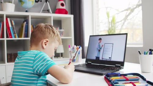 Boy is Doing His Homework at the Table Cute Child is Learning at Home with the Help of Laptop