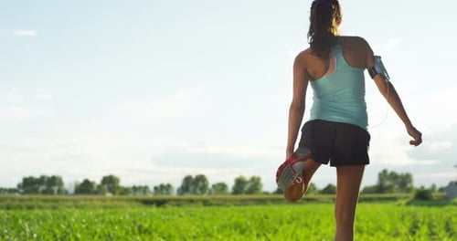 Athletic Woman Stretching Leg in Green Field