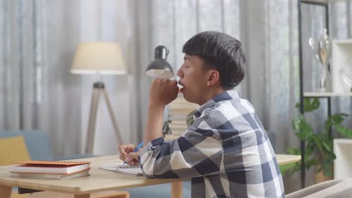 Back View Of Tired Asian Teenager Yawning While Studying At Home, Doing Home Work