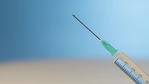 Liquid drop falling out of medical syringe, close up