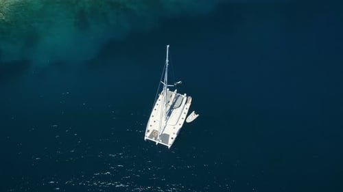 Aerial Top Down Shot of a Big White Sailing Yacht Anchored in a Bay with Man Standup Paddleboardin