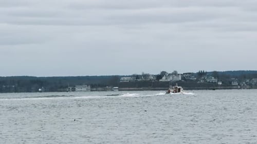 A lobstering or fishing vessel travels under full throttle across the inner harbor with a backdrop o