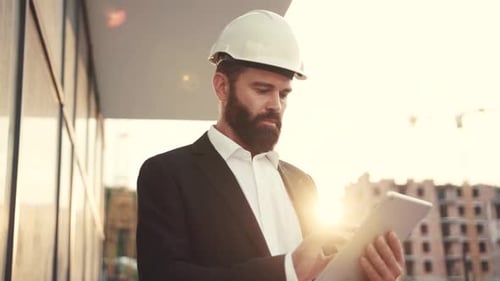 Close Up View of Handsome Bearded Engineer in a Stylish Suit and White Protective Helmet Working at