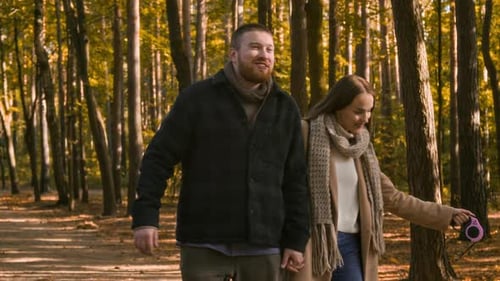 Young Couple with Dog Walking along Path in Autumn Forest
