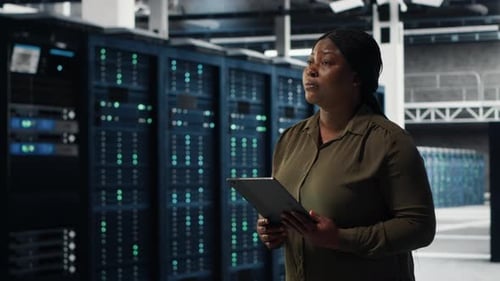Engineer with Tablet Walks Through Data Center Server Rows