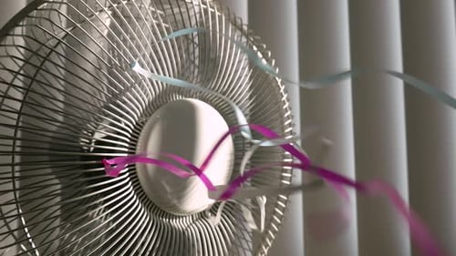 Closeup, static shot of a rotating fan with colorful ribbons on the grill, in the background closed