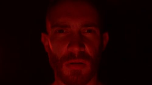 Un homme en colère regarde la caméra avec fureur et rage, son visage illuminé par les flammes de son enfer personnel