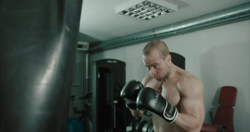 Focused male boxer punching boxing bag in indoor gym. Slow motion and close up of man at punching ba