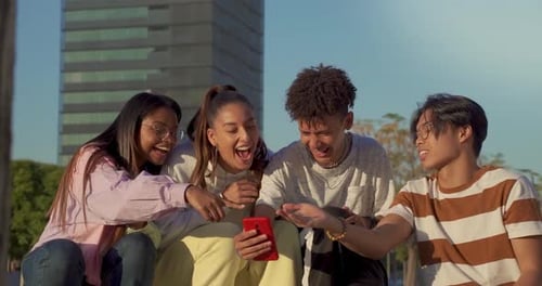 Group of Multicultural Happy Teenage Friends Looking the Phone and Laughing in a Bench in the City