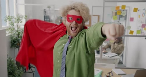 Portrait d'un employé de bureau fou dans une cape rouge et un masque, étirant le bras et agitant un costume de super-héros