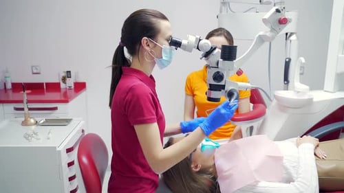 Female dentist with assistant treats teeth using a microscope in a modern dental clinic. Closeup Vie