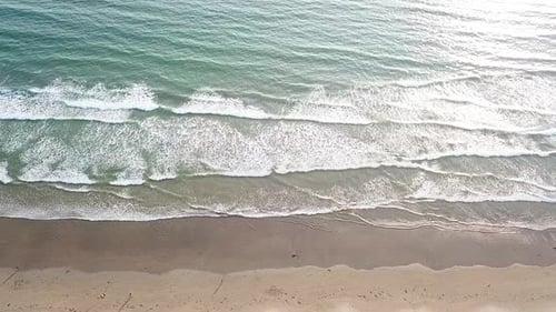 Aerial sideways view over people and waves breaking on sandy beach. Slow-motion