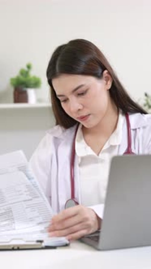 Woman Doctor Reviews Documents at Desk with Laptop