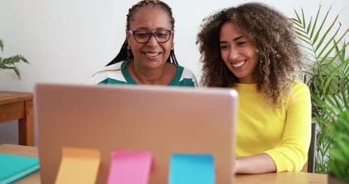 Two women smiling and using a laptop computer