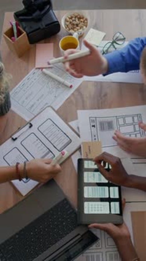Vertical of UX Designers Analyzing UI Printouts at Office Desk