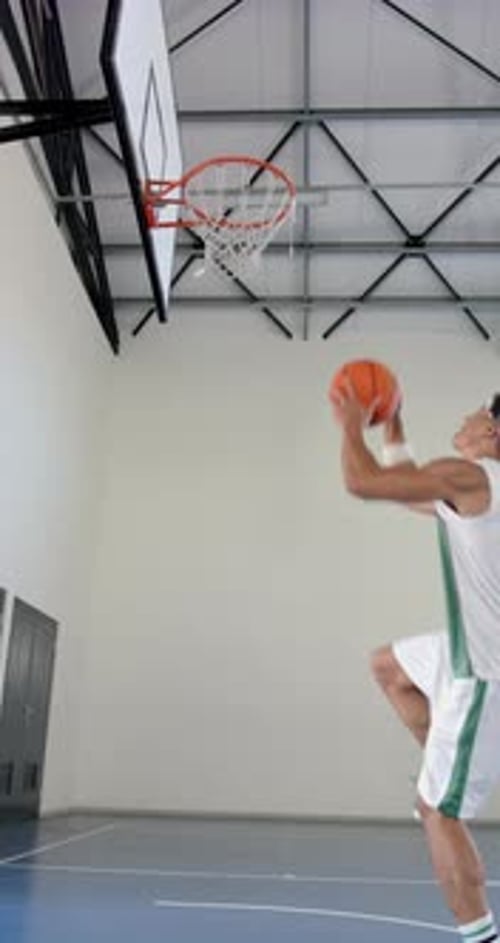 Vertical video: Playing basketball, male athlete jumping to score basket in gymnasium