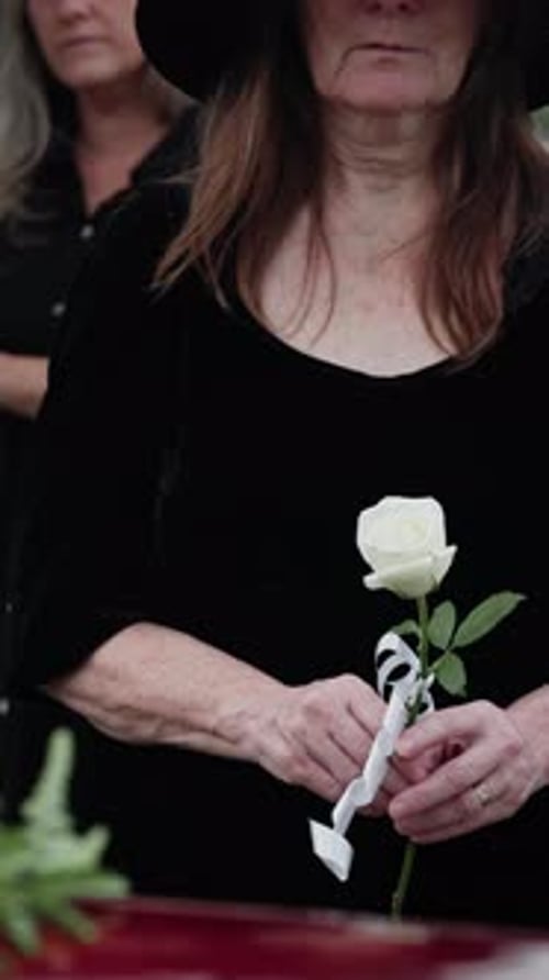 Funeral, flower and old woman in cemetery with hand, family grief and burial ceremony for final