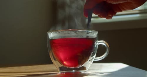 Tasse Tee auf dem Küchentisch Männerhand rührt den Tee mit einem Löffel um (Nahaufnahme)