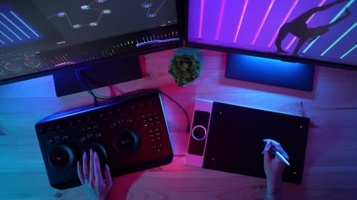 Vista superior del escritorio con luces de neón, manos de niñas, edición de vídeo en la mesa de mezclas y monitores gráficos de tabletas
