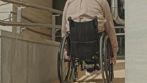 Man Riding Wheelchair on Ramp in Front of Office Building