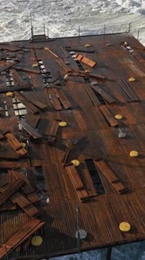 Vertical Video Coastal Clash Aerial View of Morning Storm's Waves Battling a Wooden Pier
