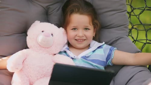 Girl Sits in a Rocking Chair Cocoon with Looks at the Tablet