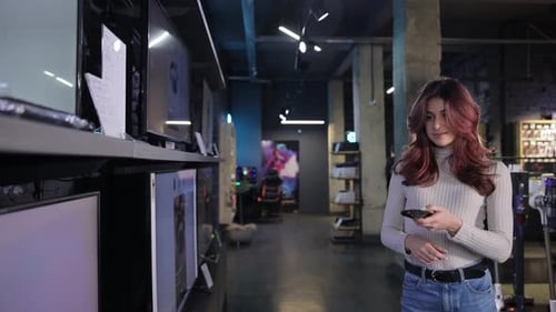 Positive Young Slim Girl Seller Turns on TV in Digital Store