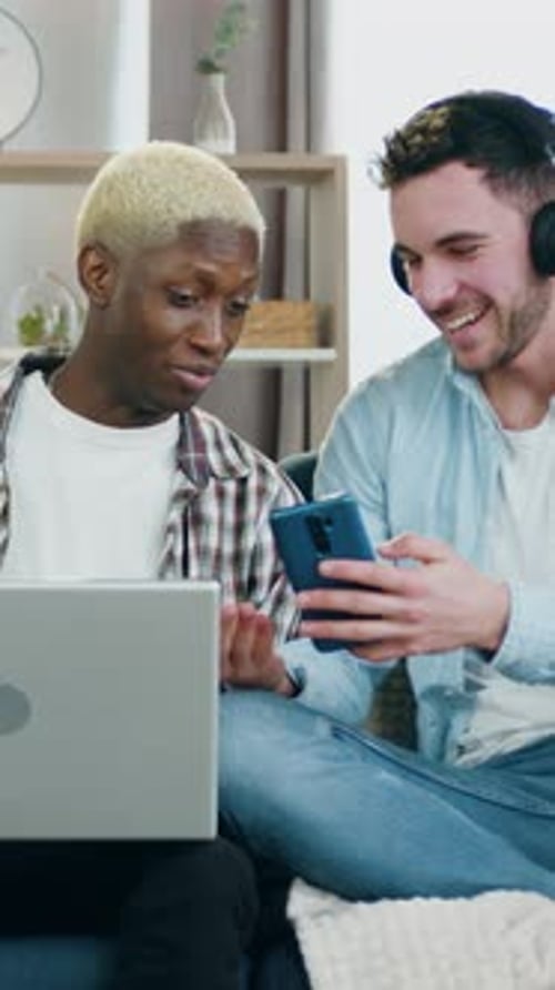 Two Young Men Laughing While Using Laptop and Phone