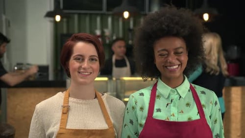 Two diverse female colleagues portraits standing inside coffee shop local business. Women employees