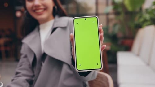 Young Woman Presenting Smartphone with Green Screen Outdoors