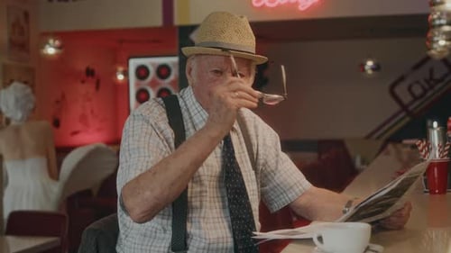 Portrait of Elderly Gentleman Taking off Glasses at Diner Counter