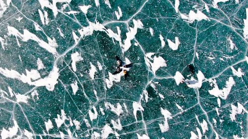 Aerial slow motion view of people ice skating on a frozen lake