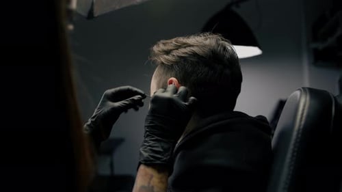 Tattoo piercing studio - a woman makes an ear piercing to a man to a guy