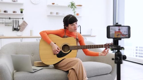 Young Adult Woman Plays Guitar to Phone Camera