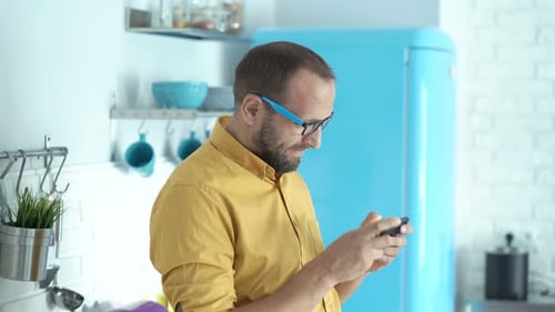 Man in Kitchen Plays Game on Mobile Phone