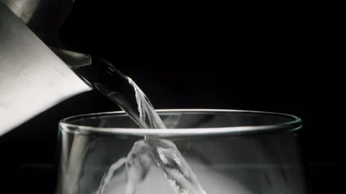 Pouring boiling water from a metal kettle into the glass. On a black background, close-up.