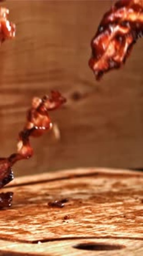 Roasted Slices of Bacon Fall on a Wooden Table Filmed on a Highspeed Camera at 1000 Fps