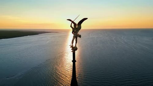 Aerial drone view of statue of Archangel Michael atop the spire of Mont-Saint-Michel at sunset in No