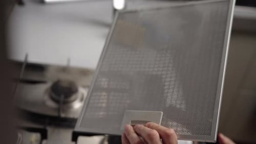 Closeup of Unrecognizable Homemaker Removing Grease Stains From Kitchen Hood Filter Using Steam