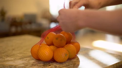 Still shot of a man grabbing an orange from a red net bag.