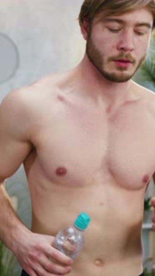 Shirtless Man Hydrating While on Treadmill at Home