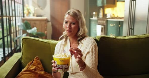Woman Eats Popcorn and Laughs on Green Sofa
