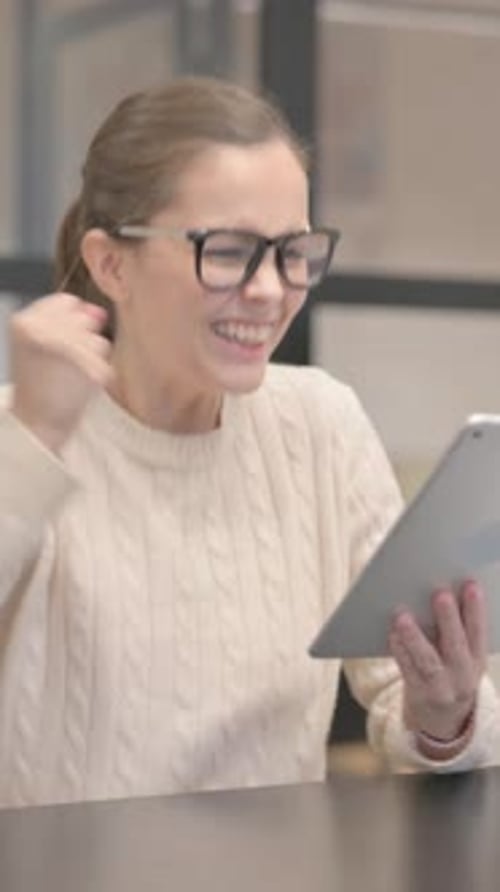 Young Woman Celebrating Success on Tablet in Office