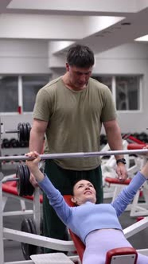 Woman Bench Pressing with Spotter in Gym